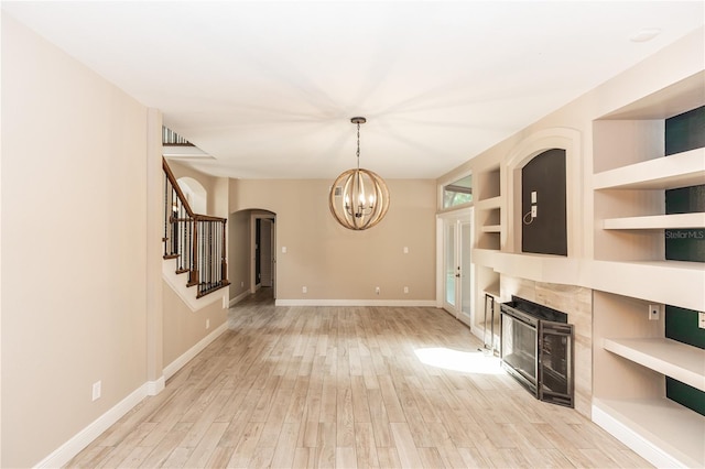 unfurnished living room with a notable chandelier, built in features, and light wood-type flooring