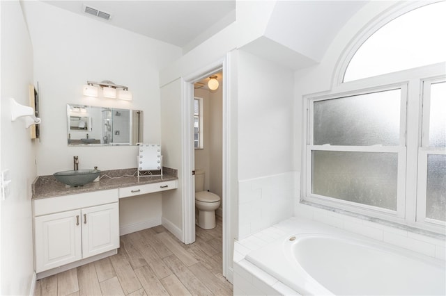 bathroom featuring vanity, hardwood / wood-style floors, tiled bath, and toilet