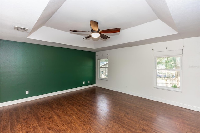 spare room with dark wood-type flooring, a wealth of natural light, ceiling fan, and a tray ceiling