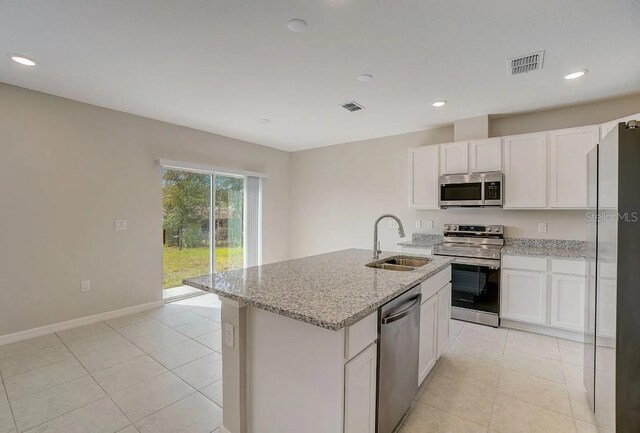 kitchen with an island with sink, appliances with stainless steel finishes, sink, and light stone counters