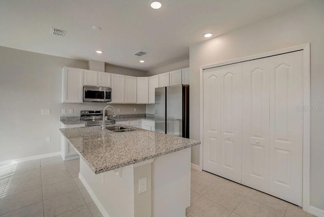 kitchen with sink, appliances with stainless steel finishes, white cabinetry, a kitchen island with sink, and light stone countertops