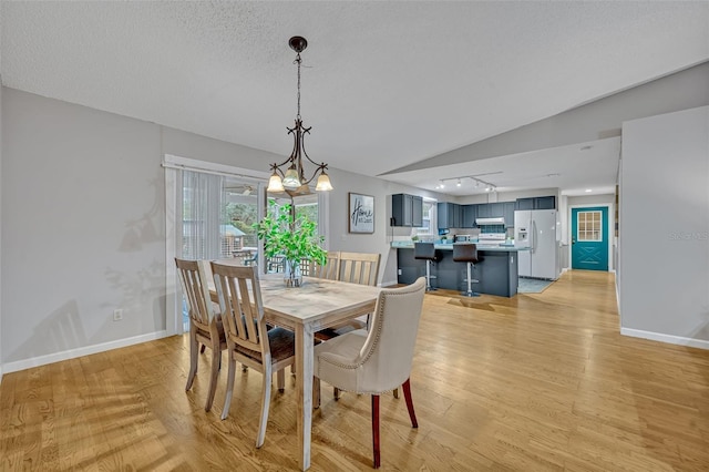 dining area featuring vaulted ceiling, track lighting, light hardwood / wood-style floors, and a textured ceiling