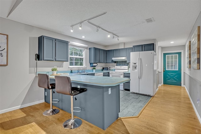 kitchen with a breakfast bar, light hardwood / wood-style flooring, a textured ceiling, kitchen peninsula, and white appliances