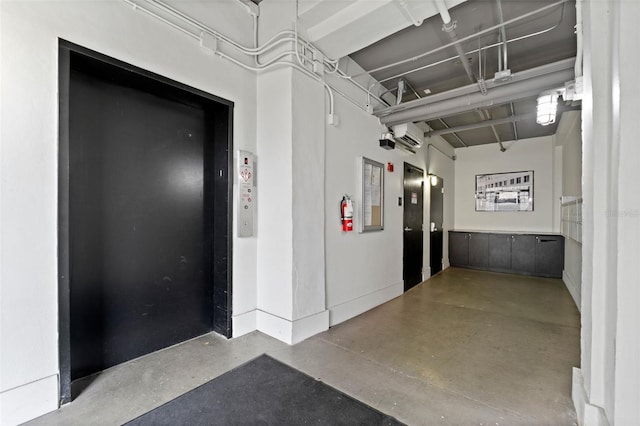 hallway featuring concrete flooring, elevator, a wall unit AC, and baseboards