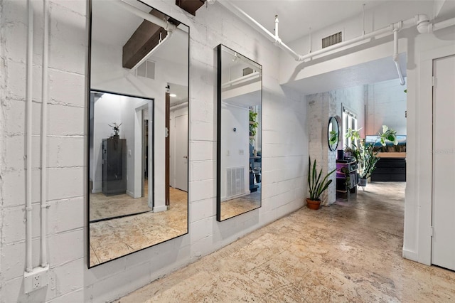 hallway with concrete block wall, concrete floors, and visible vents