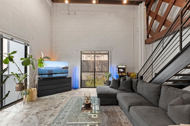 living area featuring a healthy amount of sunlight, unfinished concrete flooring, a towering ceiling, and stairs