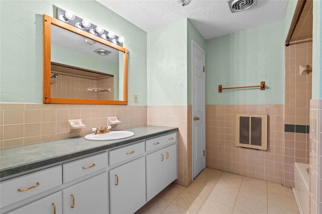 bathroom with tile walls, vanity, heating unit, a textured ceiling, and tile patterned floors