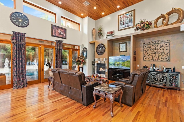 living room with wood ceiling, a towering ceiling, a healthy amount of sunlight, french doors, and light wood-type flooring