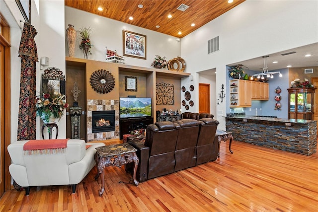 living room featuring a tile fireplace, a towering ceiling, wood ceiling, and light hardwood / wood-style flooring