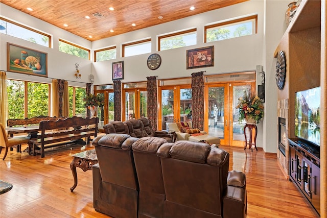 living room with wood ceiling, a towering ceiling, light hardwood / wood-style floors, and french doors