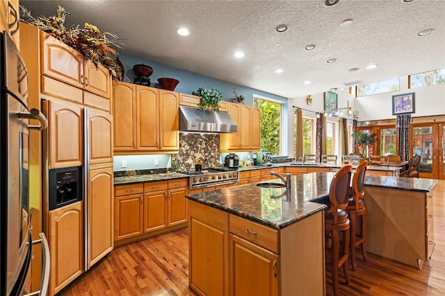 kitchen with a kitchen breakfast bar, extractor fan, a center island with sink, and dark stone countertops