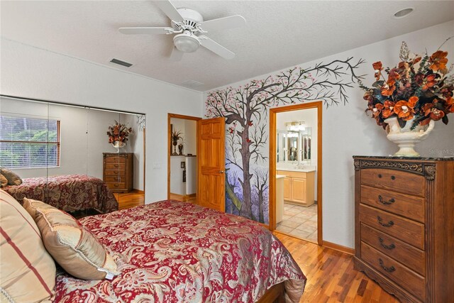 bedroom featuring ceiling fan, connected bathroom, light hardwood / wood-style floors, and a textured ceiling