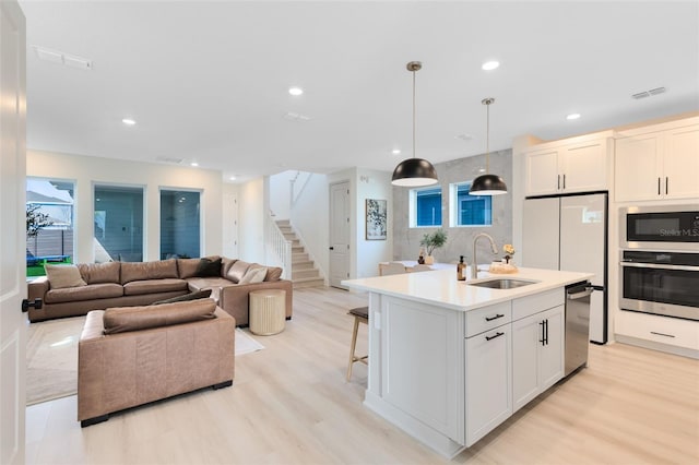 kitchen featuring pendant lighting, sink, stainless steel appliances, light hardwood / wood-style floors, and a center island with sink