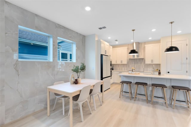 kitchen with sink, white cabinetry, hanging light fixtures, white fridge, and wall chimney range hood