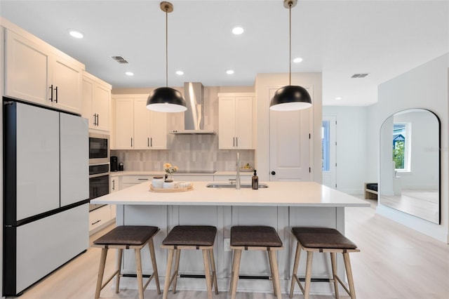 kitchen featuring pendant lighting, a kitchen island with sink, wall chimney range hood, and black appliances