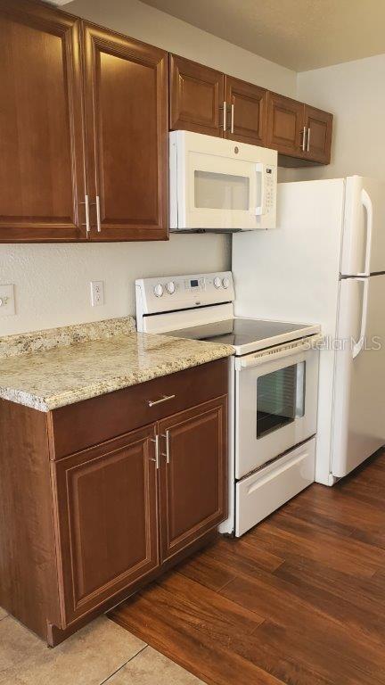 kitchen with dark hardwood / wood-style flooring, light stone counters, and white appliances