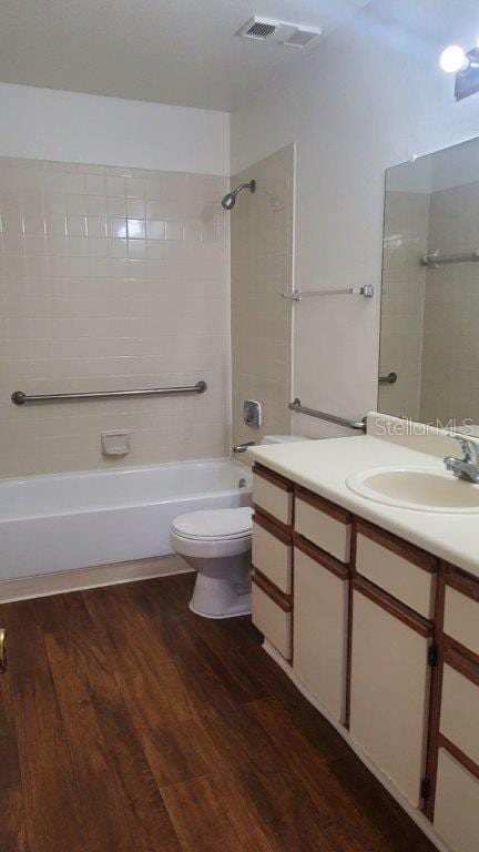 full bathroom featuring wood-type flooring, toilet, tiled shower / bath combo, and vanity