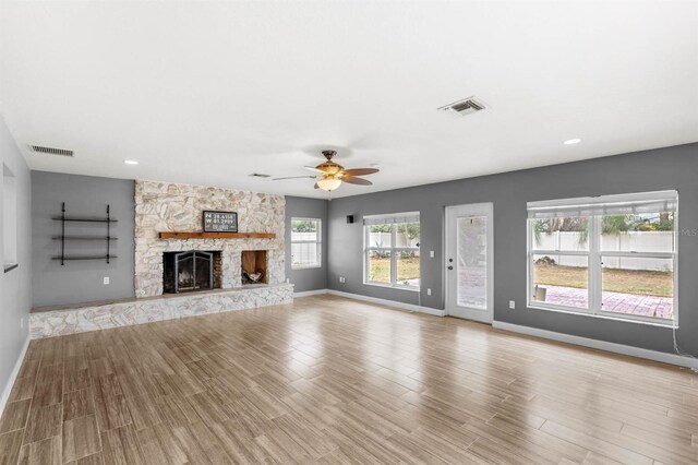 unfurnished living room featuring ceiling fan, a stone fireplace, and light hardwood / wood-style floors