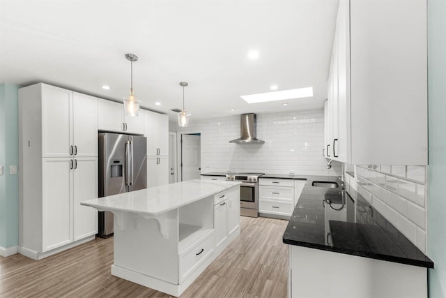 kitchen featuring wall chimney exhaust hood, white cabinetry, a center island, stainless steel appliances, and light hardwood / wood-style floors