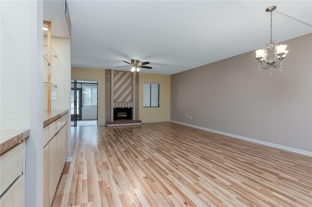 unfurnished living room with a fireplace, ceiling fan with notable chandelier, a textured ceiling, and light wood-type flooring