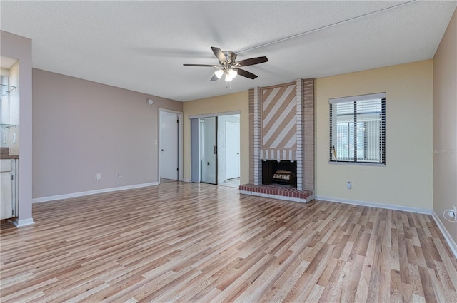 unfurnished living room with ceiling fan, a textured ceiling, a fireplace, and light hardwood / wood-style flooring