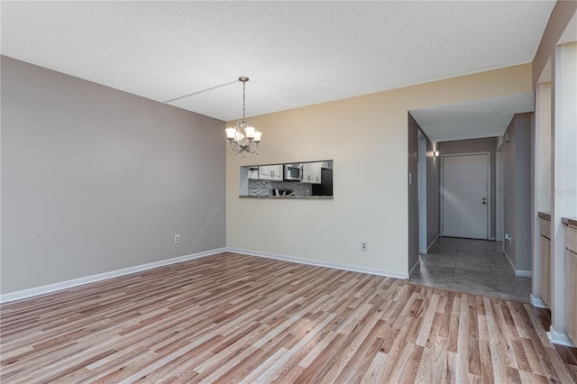 empty room with a notable chandelier, a textured ceiling, and light wood-type flooring