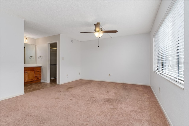 unfurnished bedroom with ensuite bath, a walk in closet, ceiling fan, light carpet, and a textured ceiling