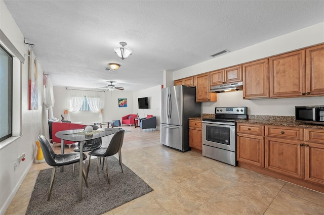 kitchen with dark stone countertops, ceiling fan, stainless steel appliances, and a textured ceiling