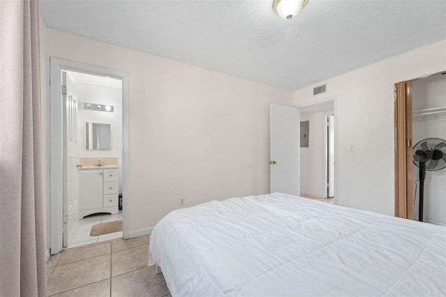 tiled bedroom featuring sink, electric panel, a textured ceiling, and ensuite bathroom