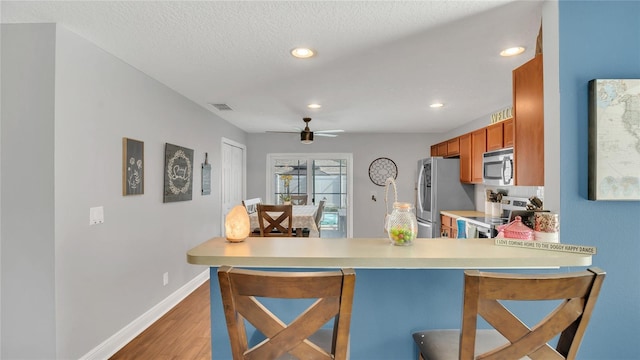 kitchen with wood-type flooring, a textured ceiling, kitchen peninsula, ceiling fan, and stainless steel appliances