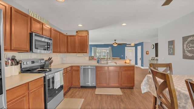 kitchen featuring sink, appliances with stainless steel finishes, decorative backsplash, kitchen peninsula, and light wood-type flooring