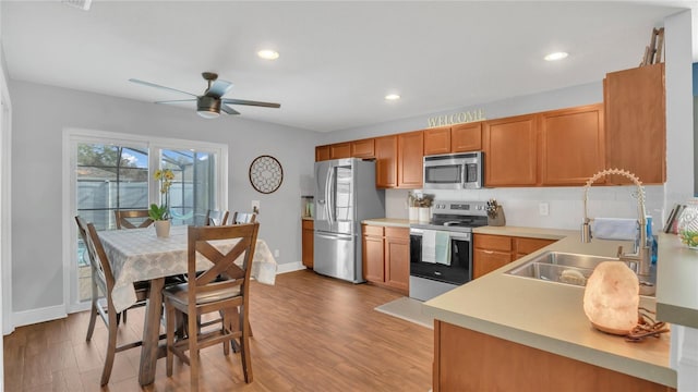 kitchen with ceiling fan, stainless steel appliances, sink, and light wood-type flooring