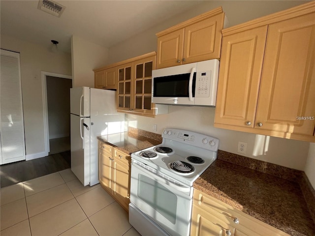 kitchen featuring white appliances, dark stone countertops, light tile patterned floors, and light brown cabinets