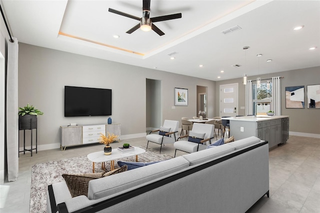 living room with ceiling fan, a tray ceiling, and sink