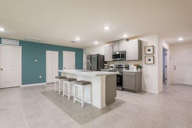 kitchen featuring a kitchen island with sink, gray cabinets, a breakfast bar, and appliances with stainless steel finishes