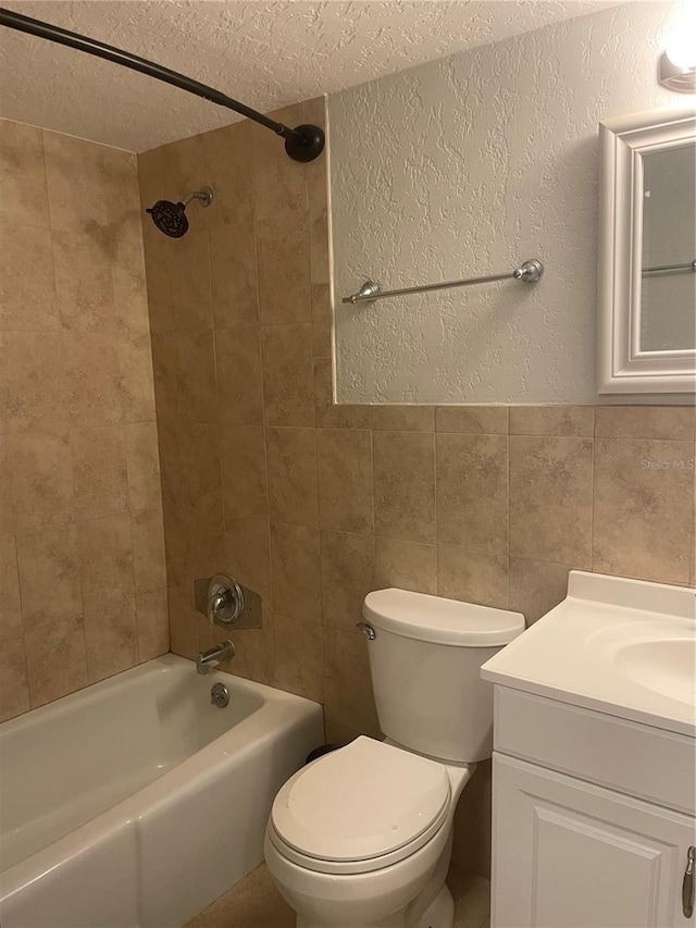 full bathroom featuring tile walls, tiled shower / bath combo, vanity, a textured ceiling, and toilet