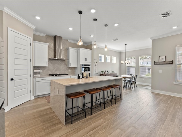 kitchen featuring an island with sink, a breakfast bar area, white cabinets, stainless steel appliances, and wall chimney range hood