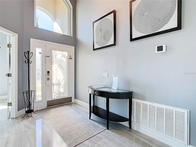 foyer entrance featuring a towering ceiling, baseboards, and visible vents