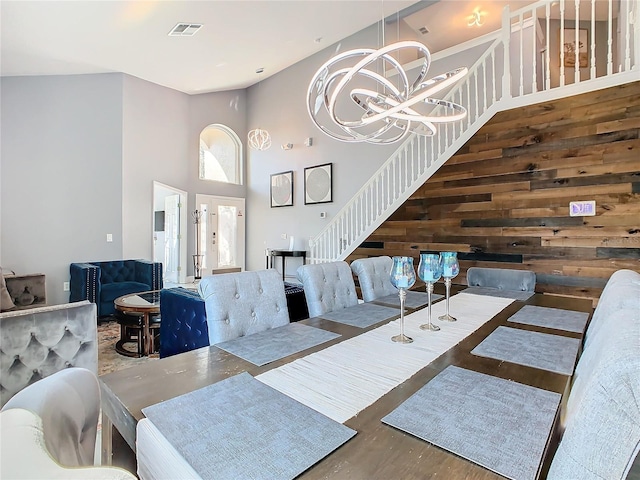 dining room with wooden walls, visible vents, wood finished floors, a high ceiling, and a chandelier