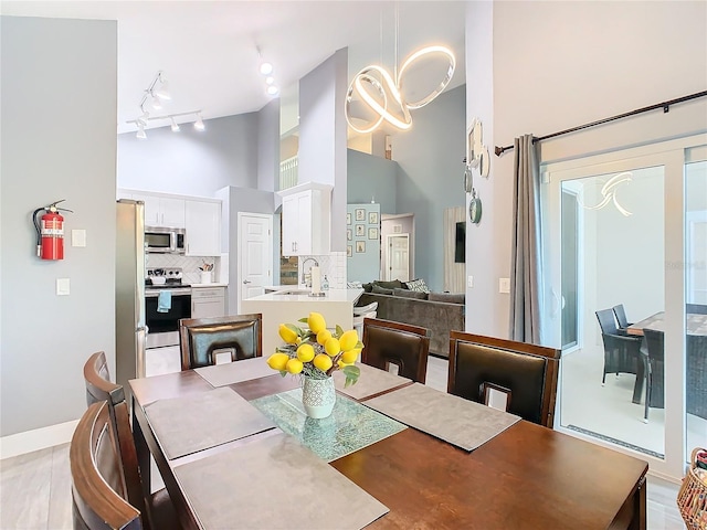 dining room featuring high vaulted ceiling, rail lighting, and baseboards