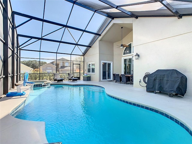 view of pool featuring glass enclosure, a patio, a pool with connected hot tub, a ceiling fan, and grilling area