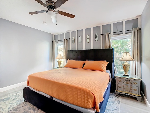 bedroom with a ceiling fan, multiple windows, baseboards, and wood finished floors