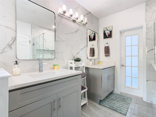 full bathroom with tile walls, a marble finish shower, and vanity