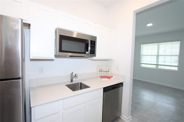 kitchen with baseboards, light countertops, stainless steel appliances, white cabinetry, and a sink