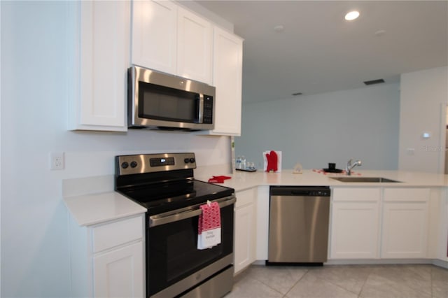 kitchen with light countertops, appliances with stainless steel finishes, a peninsula, white cabinets, and a sink