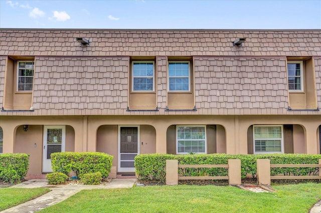 view of property with mansard roof, a front yard, and stucco siding