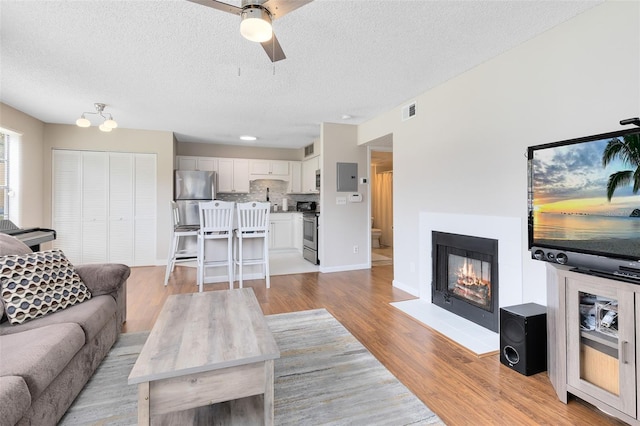 living room featuring ceiling fan, electric panel, a textured ceiling, and light wood-type flooring