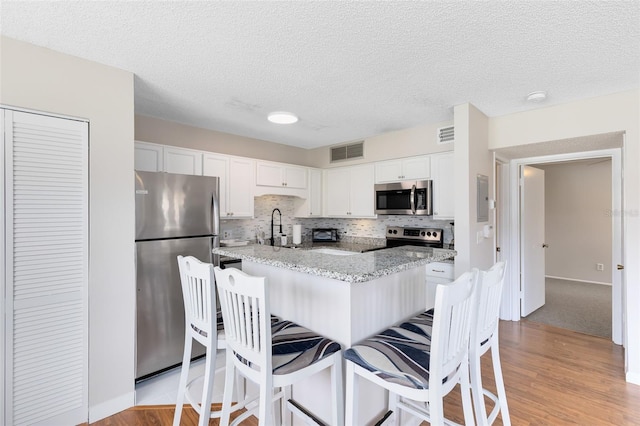 kitchen featuring a breakfast bar area, appliances with stainless steel finishes, white cabinetry, tasteful backsplash, and light stone countertops