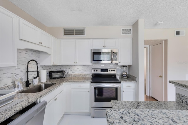 kitchen with appliances with stainless steel finishes, light stone countertops, sink, and white cabinets