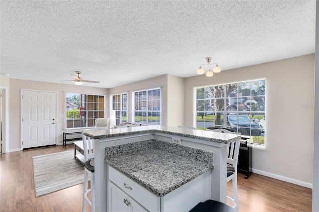 kitchen featuring white cabinetry, ceiling fan with notable chandelier, light stone counters, and light wood-type flooring